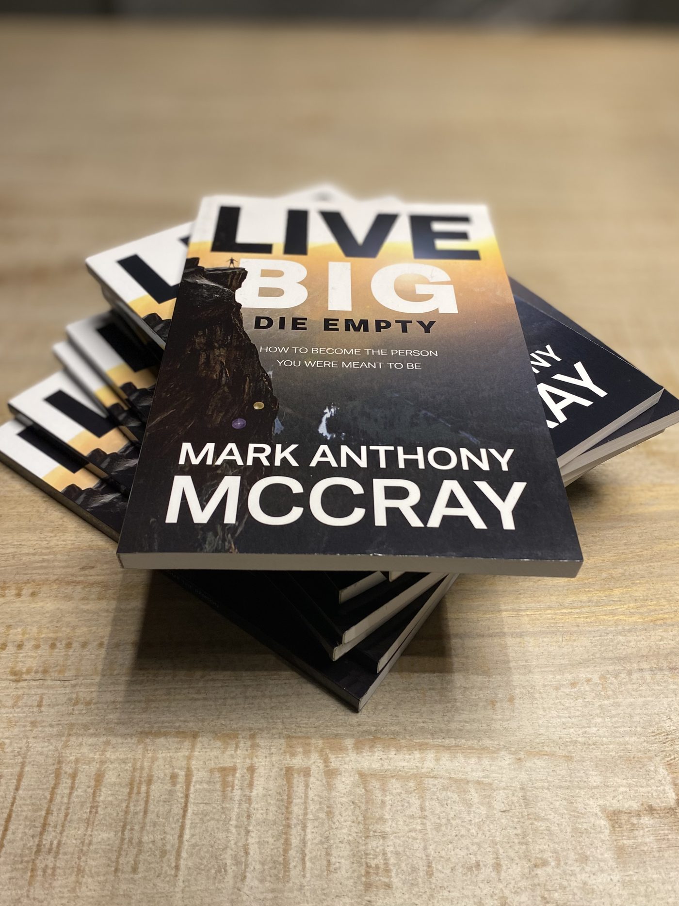 A stack of Live BIG! Die Empty paperbacks on a wooden surface